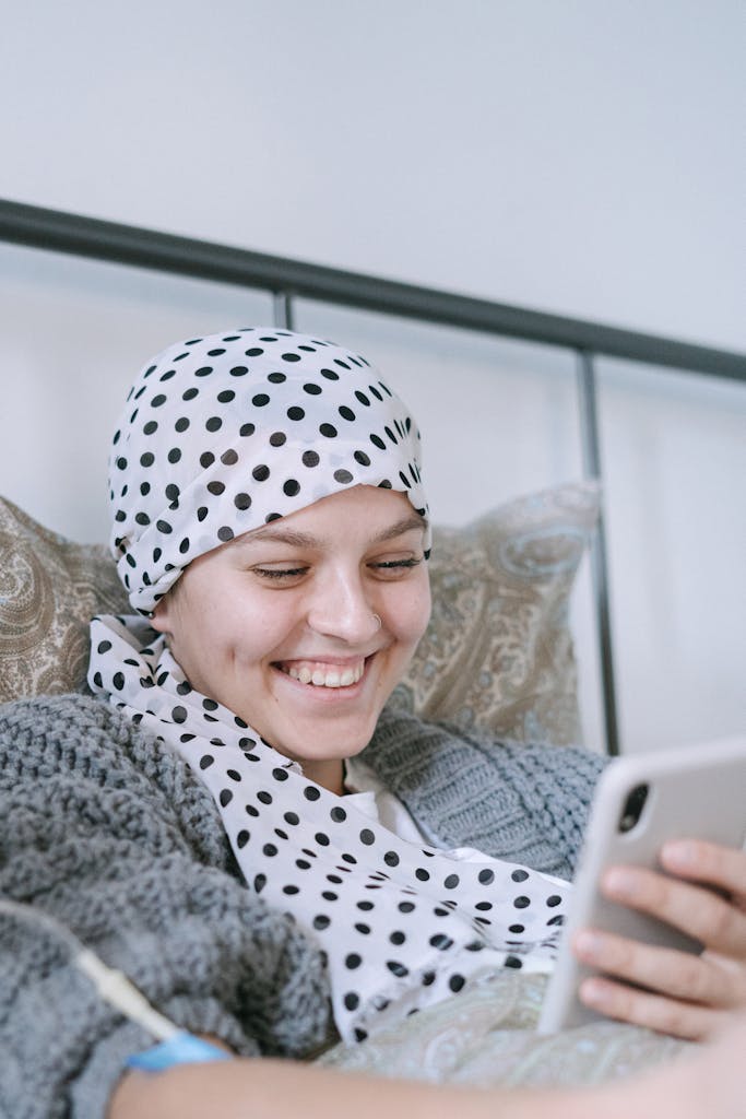 A woman with a polka dot scarf smiles while using her smartphone in bed.