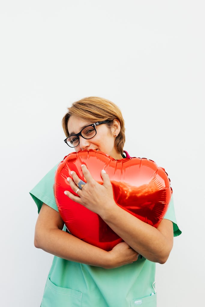 Smiling healthcare worker embraces a red heart-shaped balloon, symbolizing care and compassion.