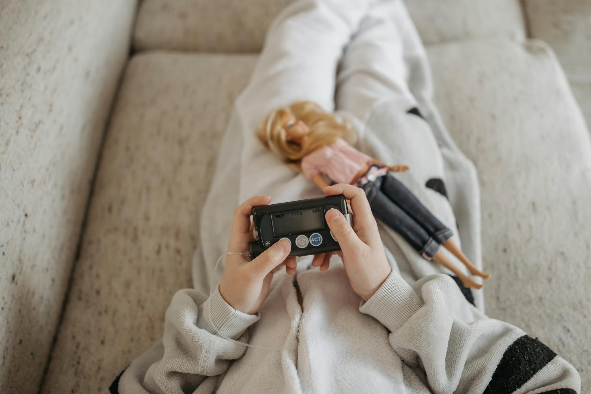 Close-up of a child holding an insulin pump with a doll resting on their lap, symbolizing diabetes management in daily life.