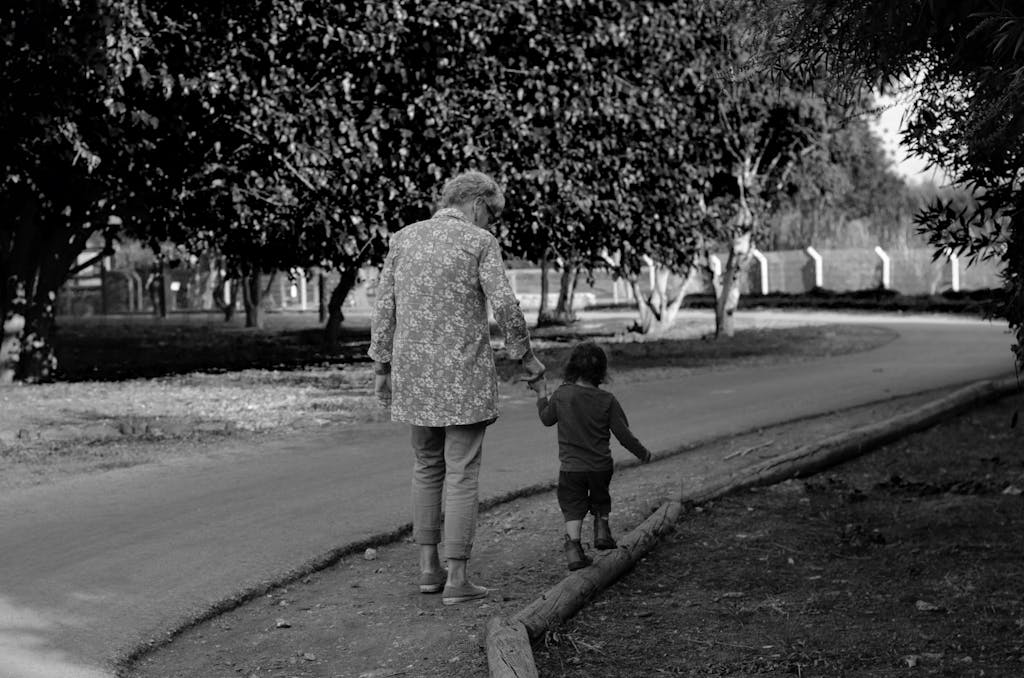A touching black and white photo of a grandmother and grandchild holding hands on a park path.