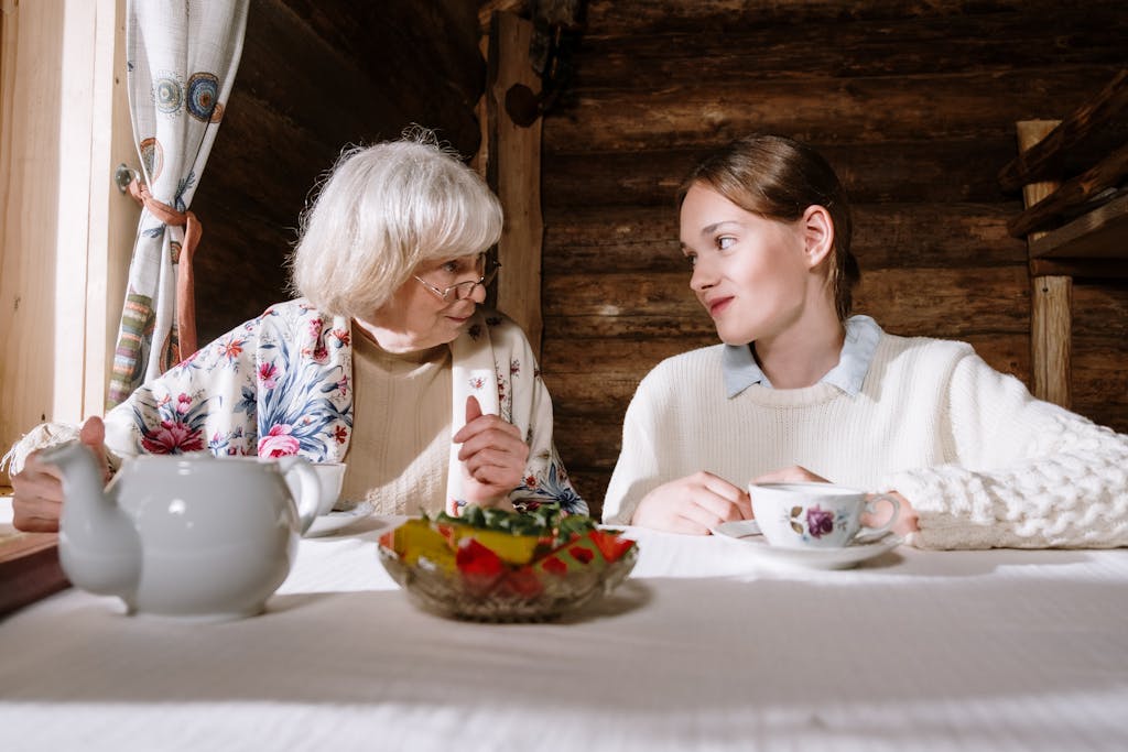 A senior adult and teenager sharing a cozy teatime conversation indoors.