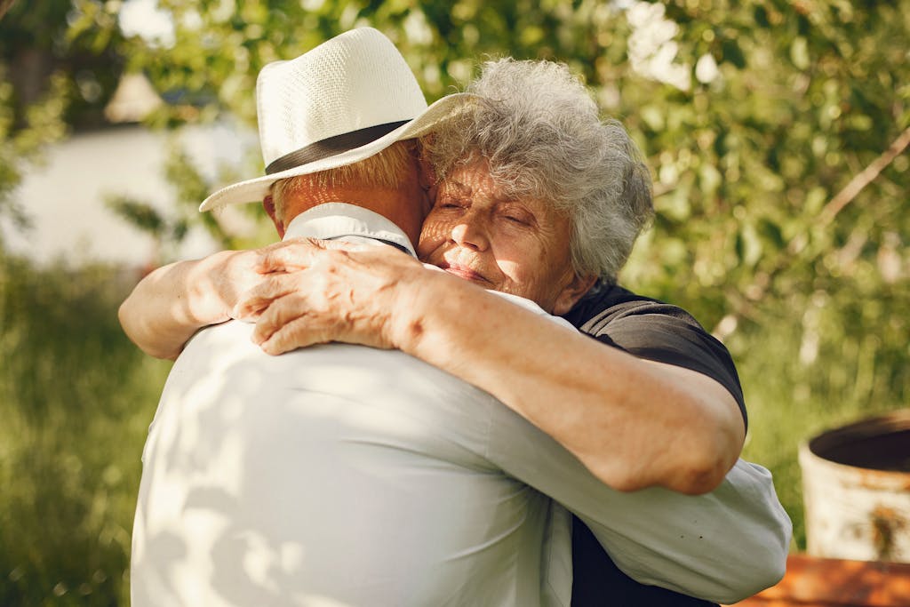 An elderly couple sharing a warm embrace in a sunny outdoor setting.