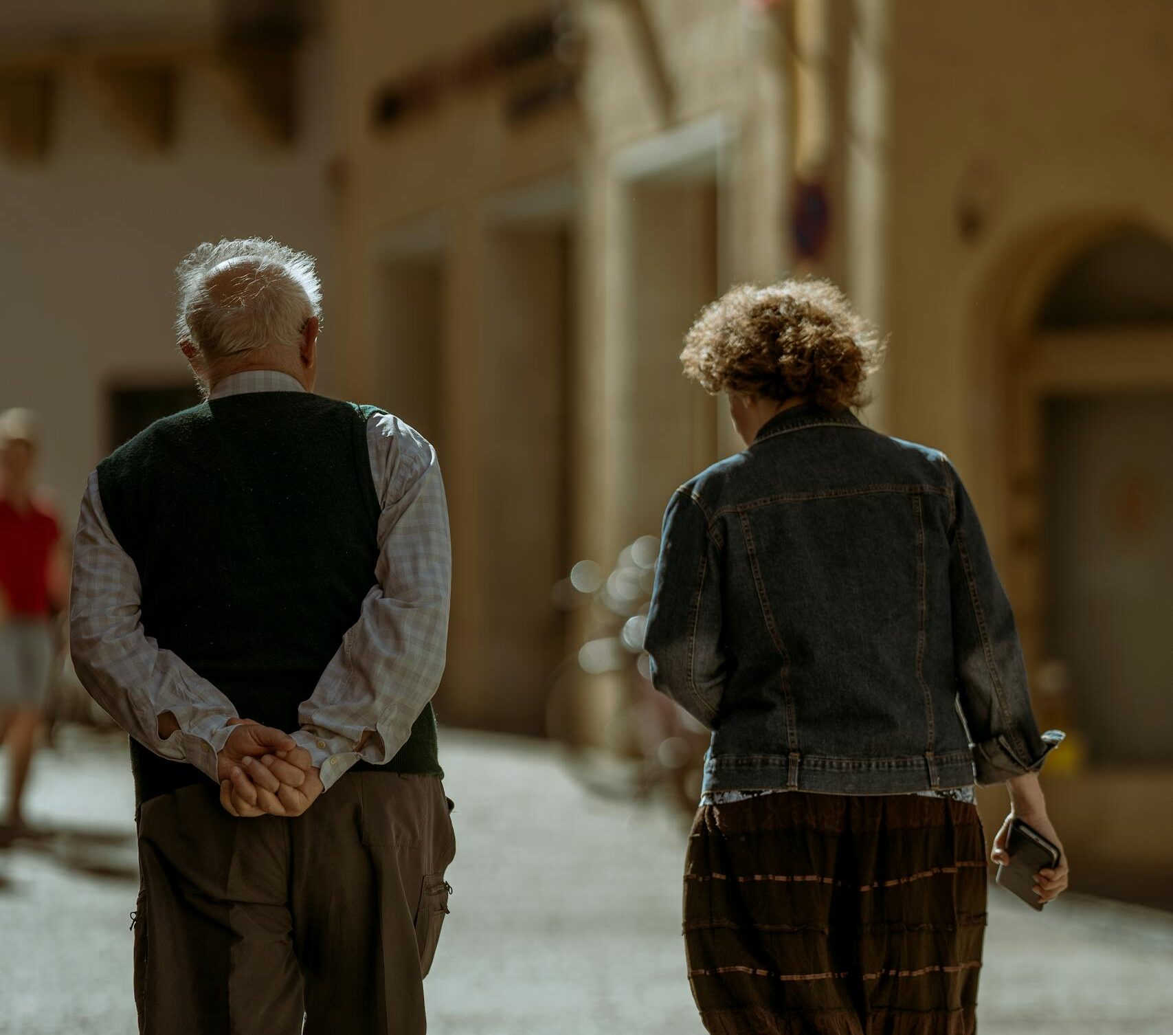 Senior couple walking together down a sunlit street with a sense of companionship.