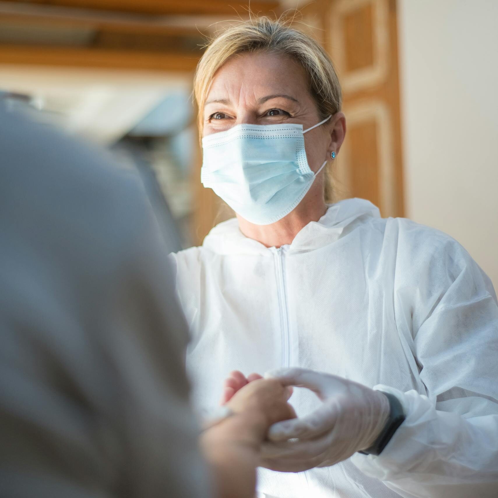 A healthcare worker in full protective gear providing care to a patient indoors.