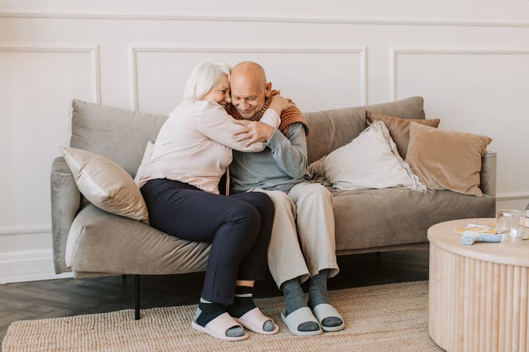 Tender moment of affection between a senior couple embracing on a comfortable couch indoors.