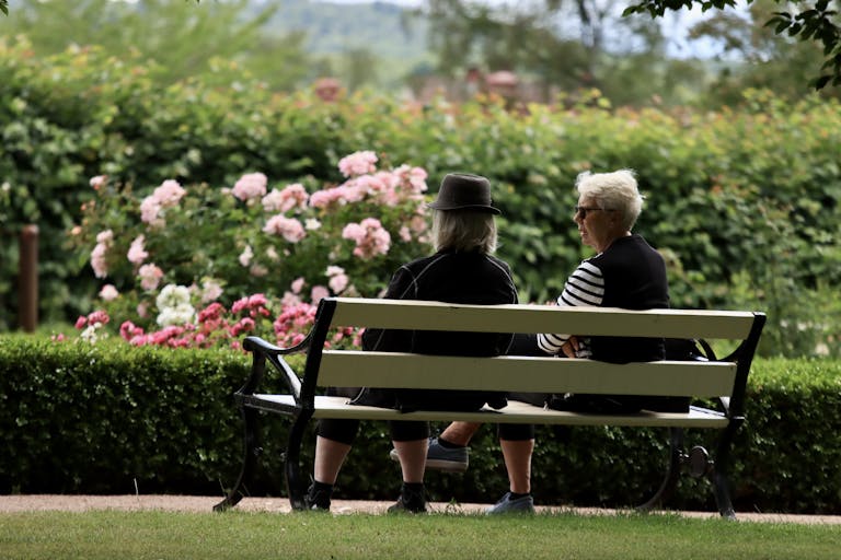 Two senior adults conversing on a bench in a flower garden in Jönköping, Sweden.