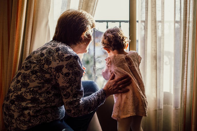 A loving moment between grandmother and grandchild near a window filled with sunlight.