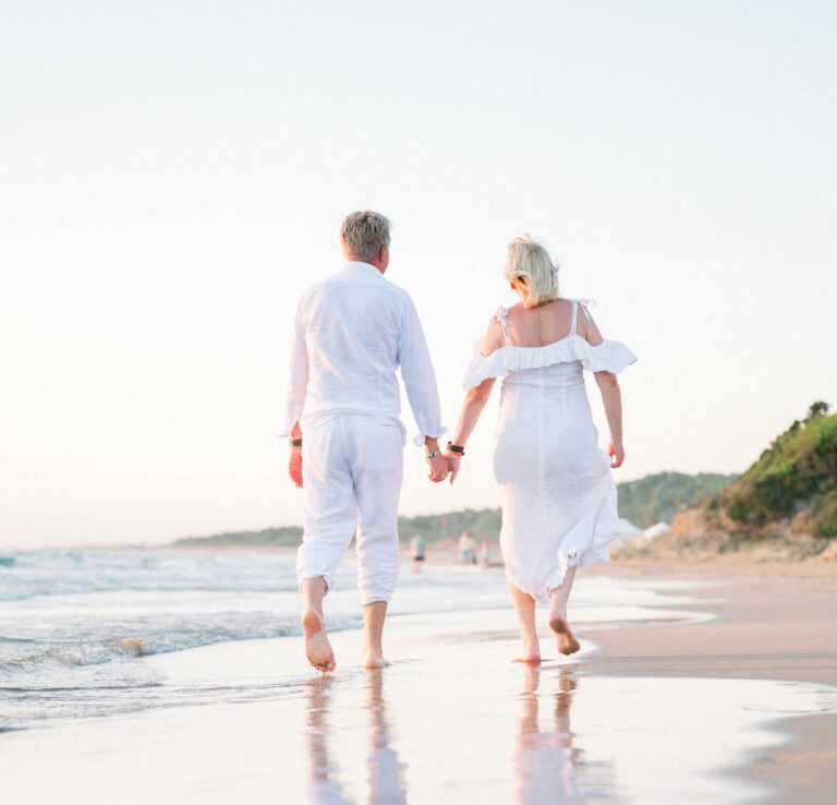 Elderly couple holding hands, walking along the beach at sunset, reflecting love and tranquility.
