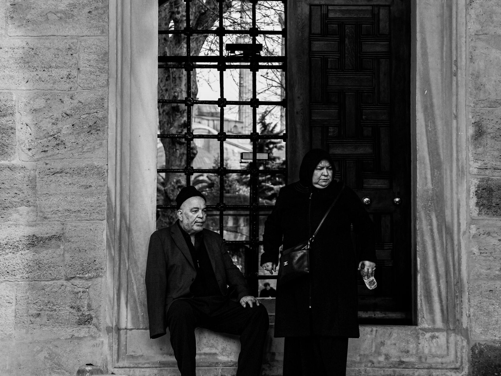 Black and white photo of an elderly couple by a historical wooden door.