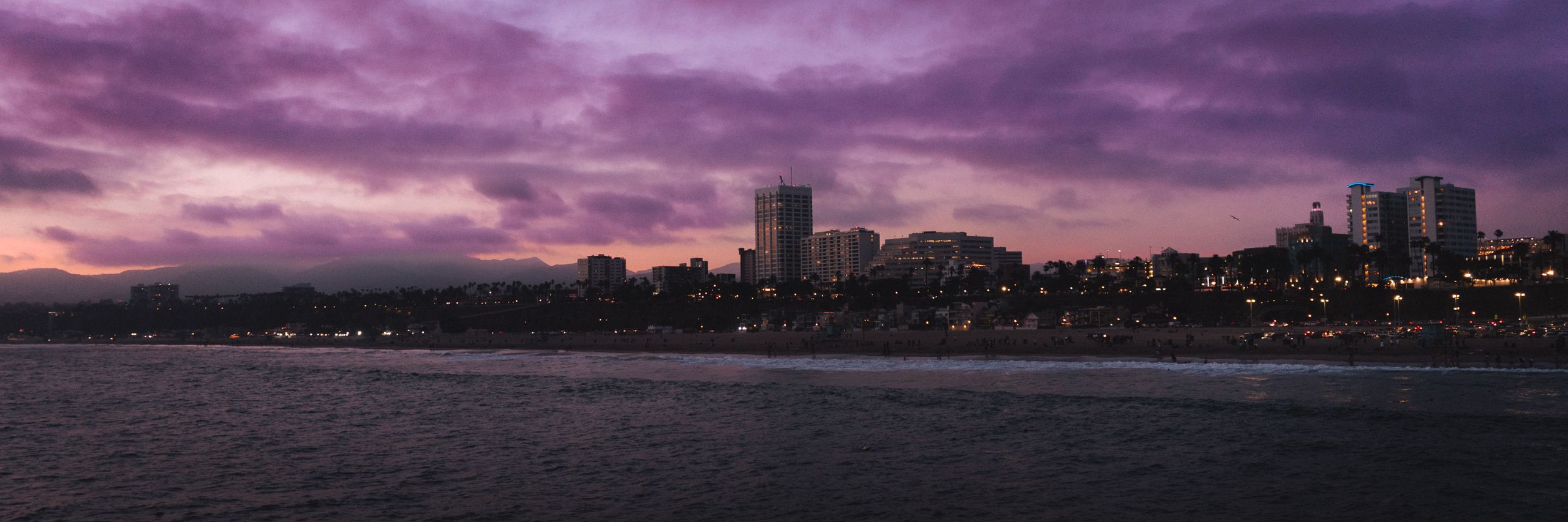 Dramatic sunset over a coastal city with a vibrant purple sky and waterfront.